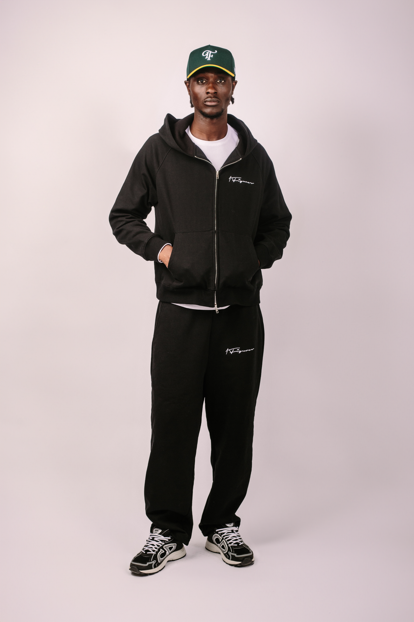 Amin wearing a black tracksuit with visible 1FIGURES branding on a white background